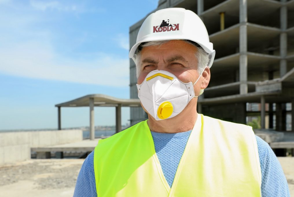 Image: a construction worker follows social distancing guidelines by wearing a mask on a job site.