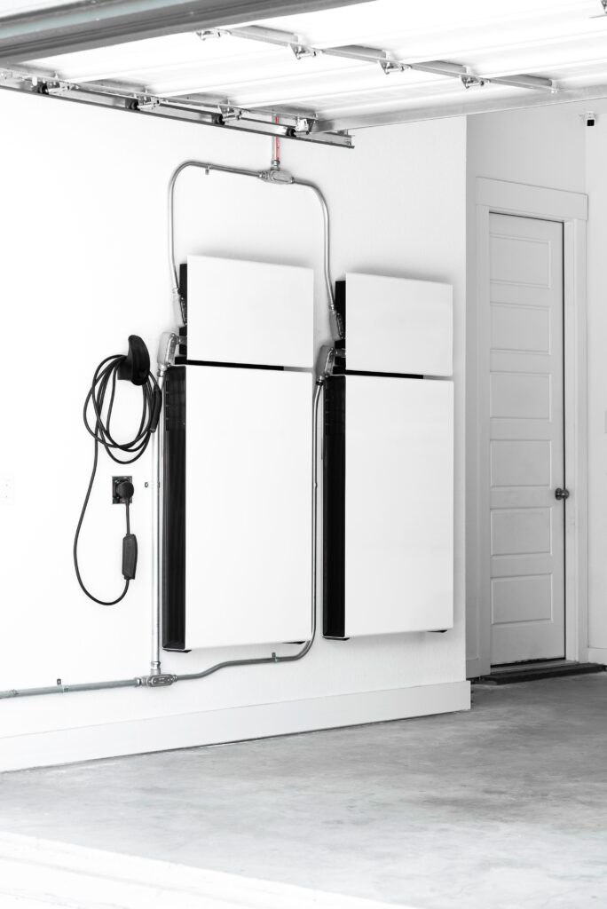 Two battery backups hang on a garage wall with a charging cable attached for an electric vehicle. 